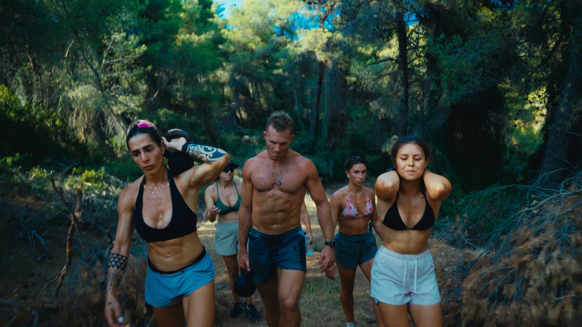 Residents hiking uphill through the forest carrying kettlebells